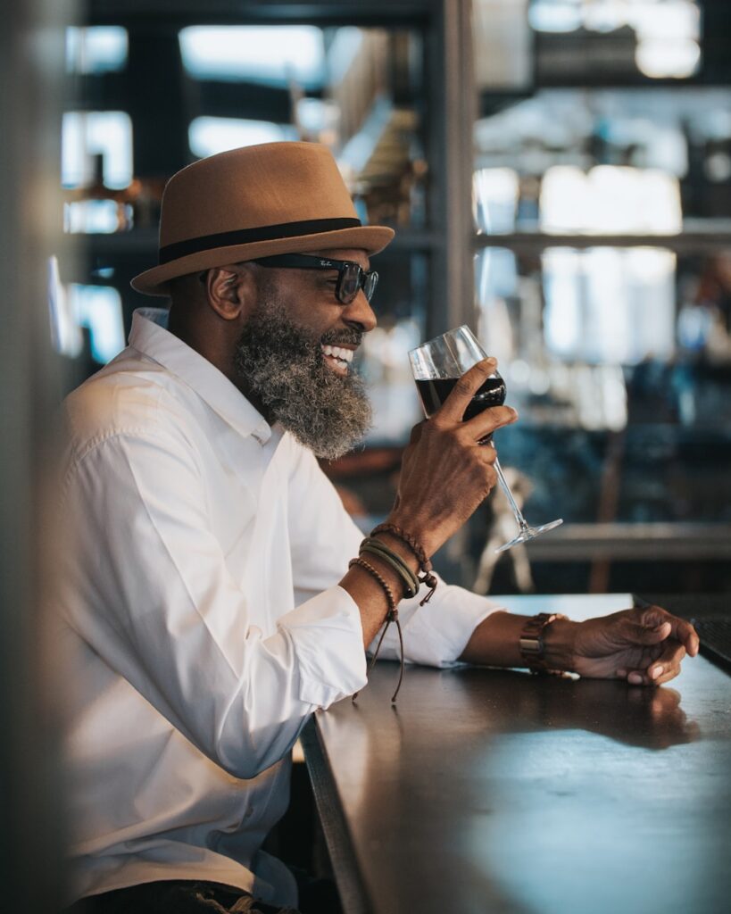 Photo by Joey Nicotra man in white dress shirt and brown hat holding clear drinking glass